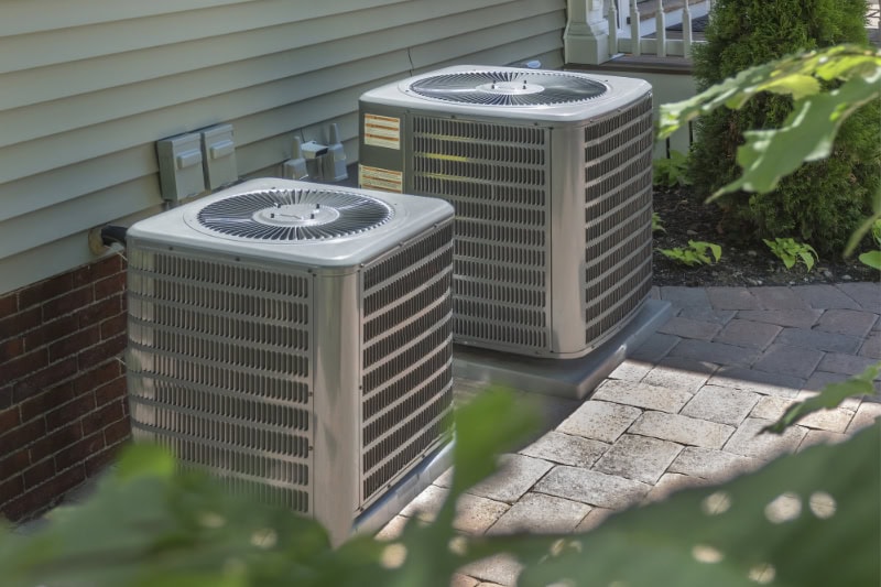 Two air conditioner units sitting side by side outside of a house.