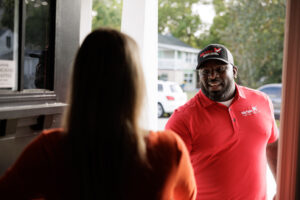 A McVay home service technician in a red branded polo and cap greets a customer at her front door in Glenshaw.