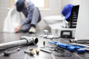 Plumber kneeling beside a toilet with plumbing tools and fittings on the floor in a Verona, PA home.
